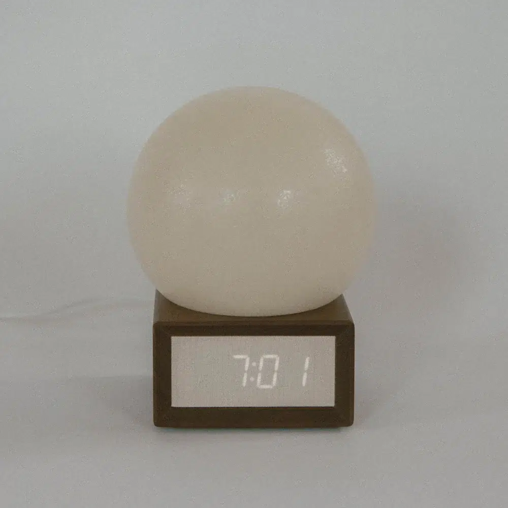 A round, white lamp sits on a wooden digital clock displaying the time 7:01. The background is plain and light-colored.
