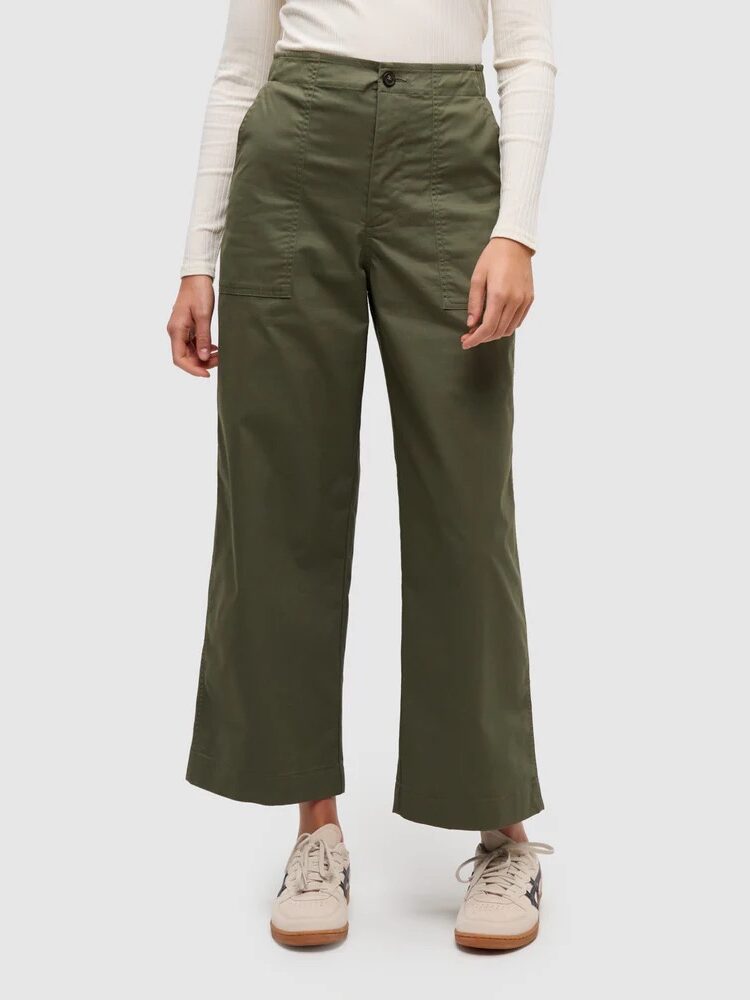 Person wearing high-waisted, wide-leg olive green pants, a long-sleeve white top, and beige sneakers, standing against a plain background.