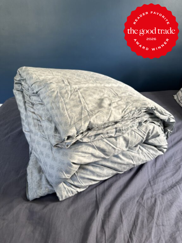 A folded light gray comforter sits on a dark gray bedspread; a red badge in the corner reads "The Good Trade Reader Favorite Award Winner 2026.