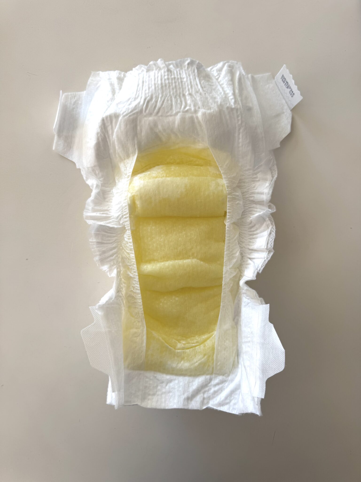 An open, unused disposable diaper with a yellow inner absorbent pad is displayed on a light surface.