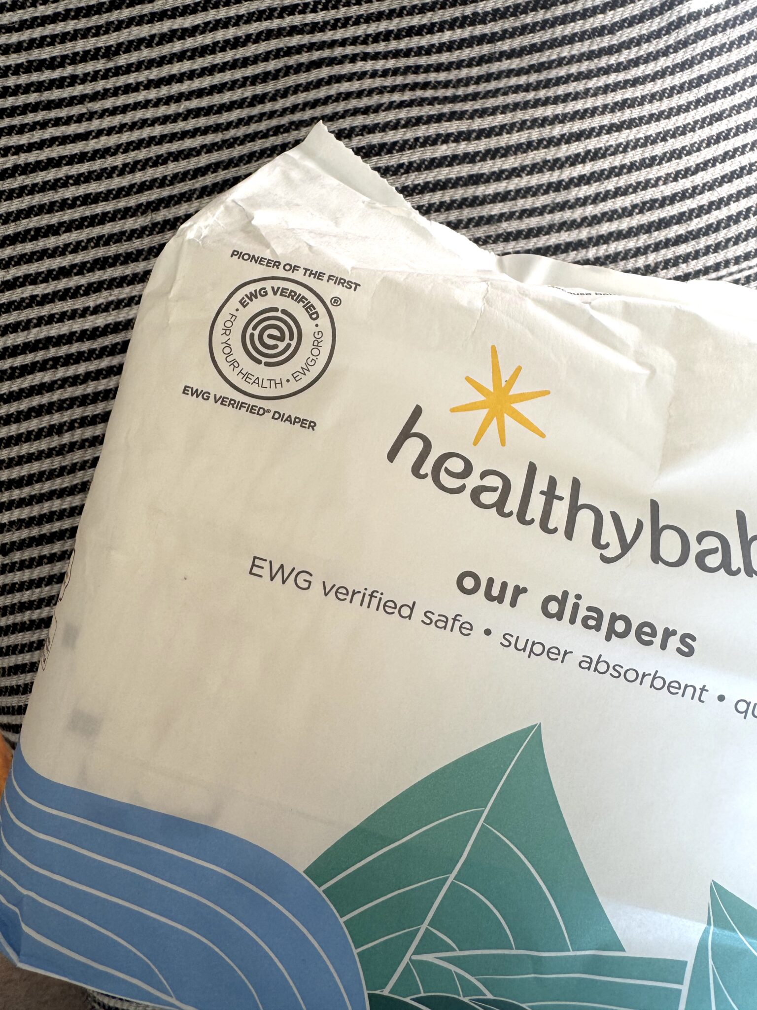 A pack of healthybaby brand diapers with EWG Verified and "for your health" logos on white packaging, placed on a striped fabric surface.