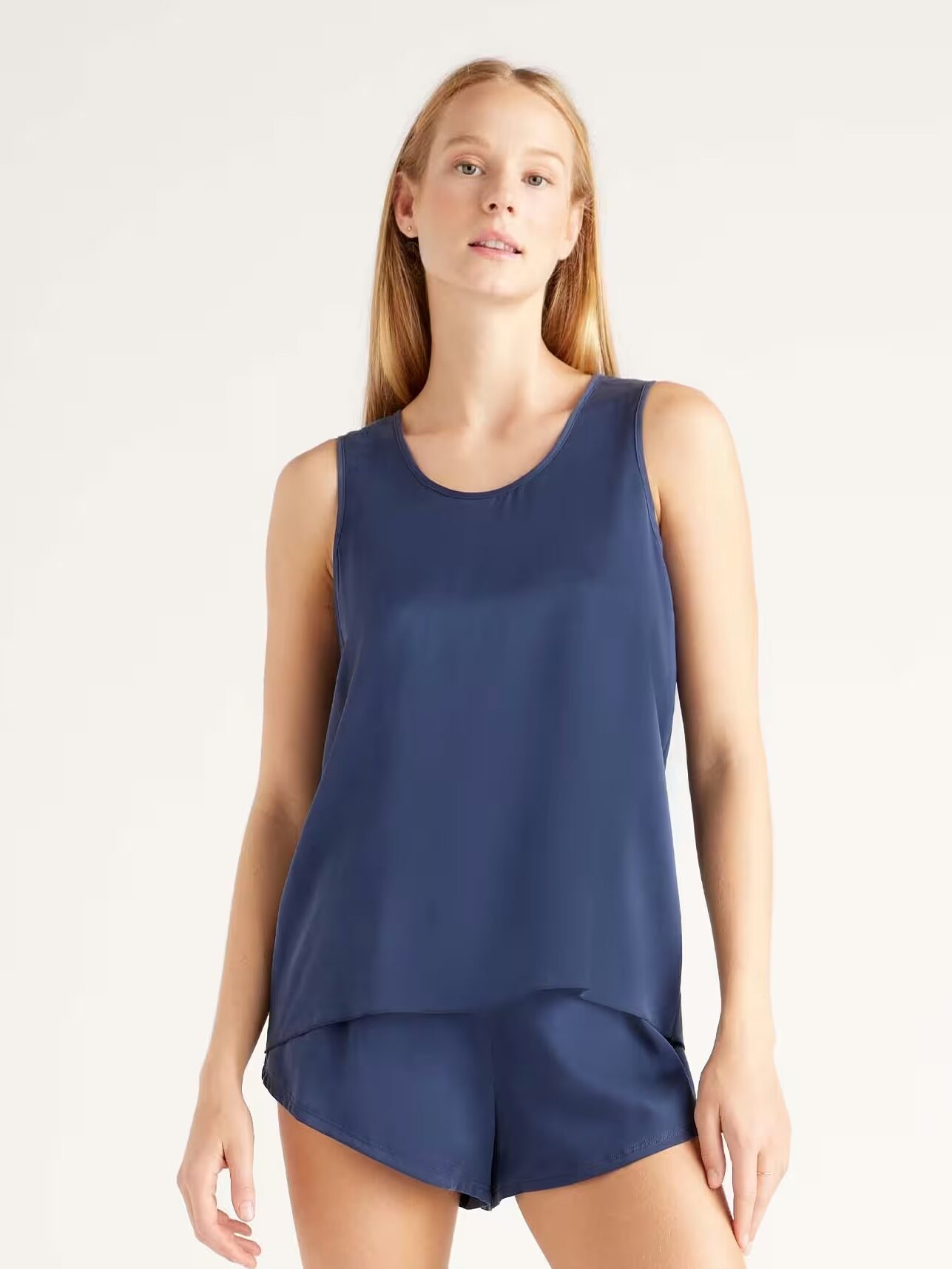 A woman stands wearing a sleeveless navy blue top and matching shorts, facing forward against a plain light background.