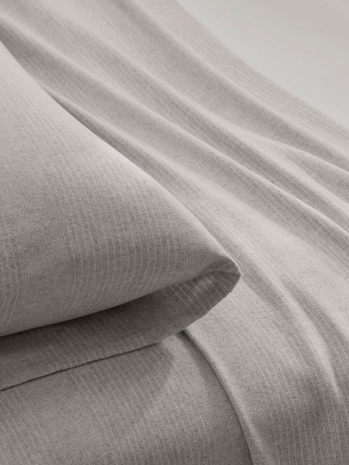 Close-up of a neatly made bed with light gray, subtly striped bedding, including a pillow and a draped sheet.