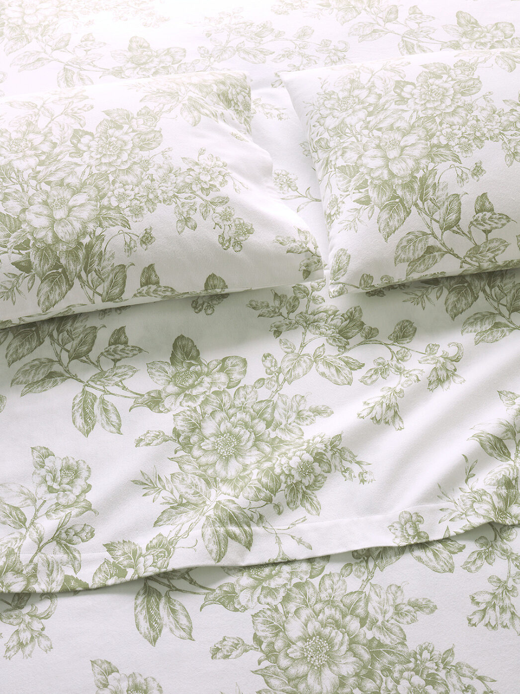 White bed sheets and pillowcases with a green floral pattern.