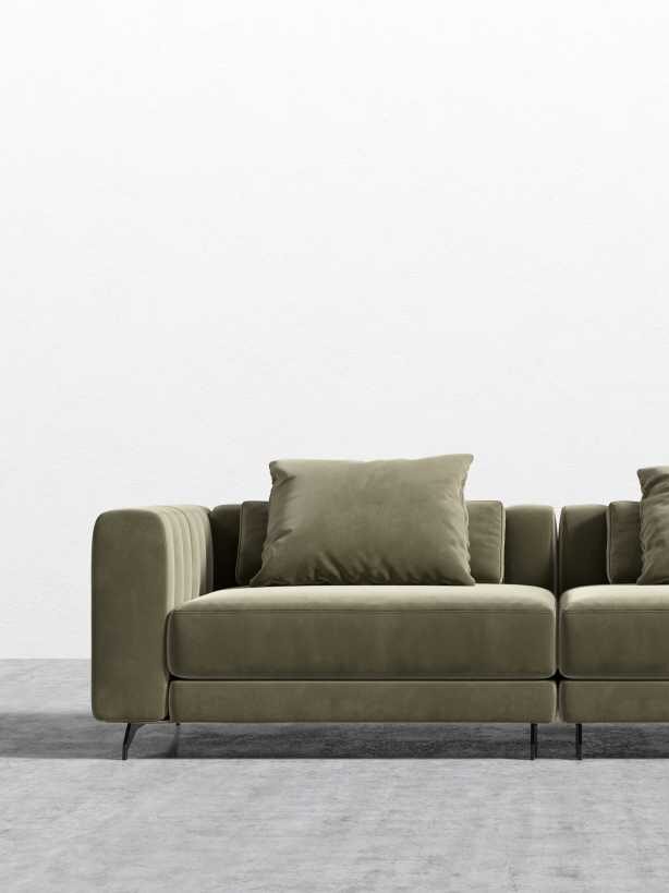 A modern olive green velvet sofa with two seat cushions and two matching back pillows, placed on a gray concrete floor against a plain white wall.