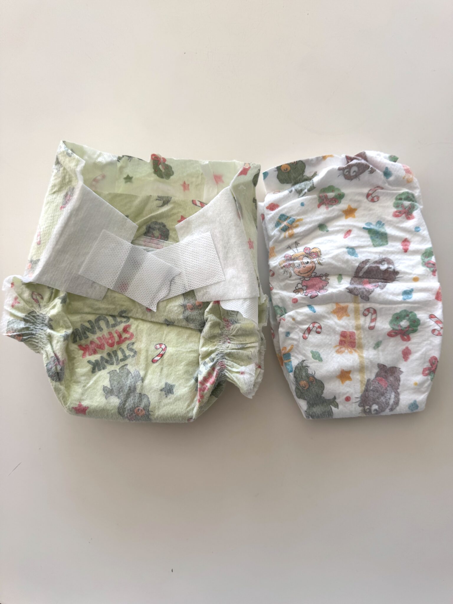 Two disposable baby diapers with cartoon animal prints lie side by side on a white surface; one diaper is open and the other is folded.