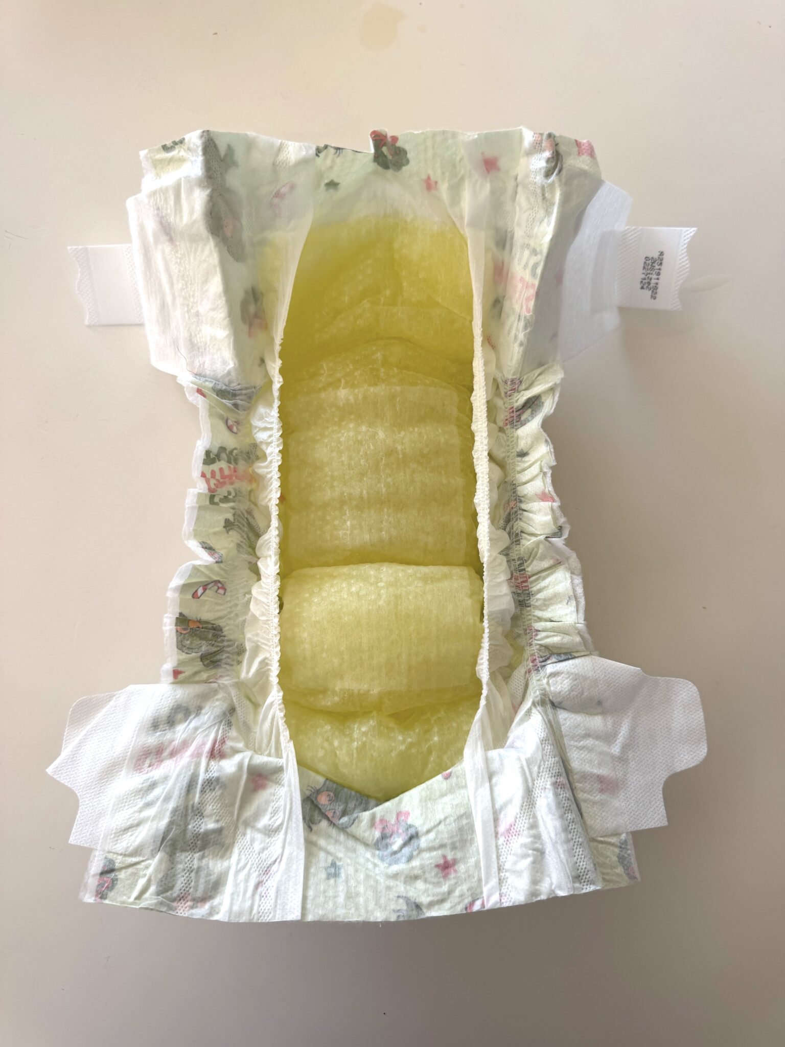 An open disposable diaper on a flat surface, showing a yellow-stained absorbent area in the center.