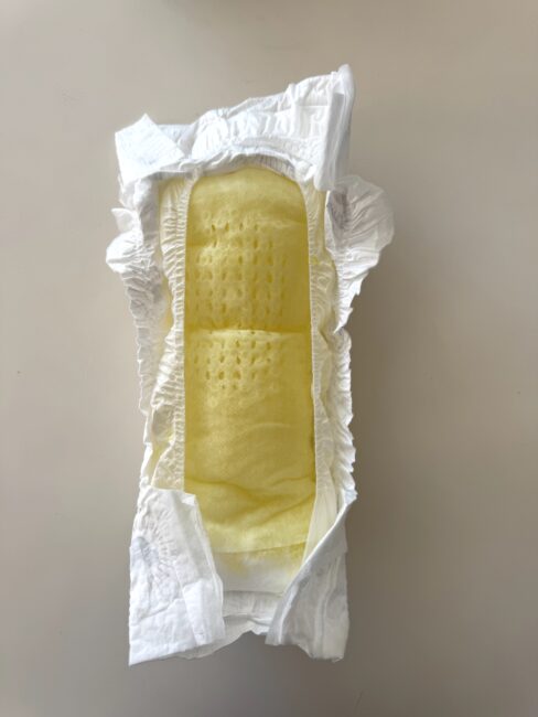 A disposable diaper lying open on a flat surface, displaying its yellow absorbent inner layer and elastic edges.