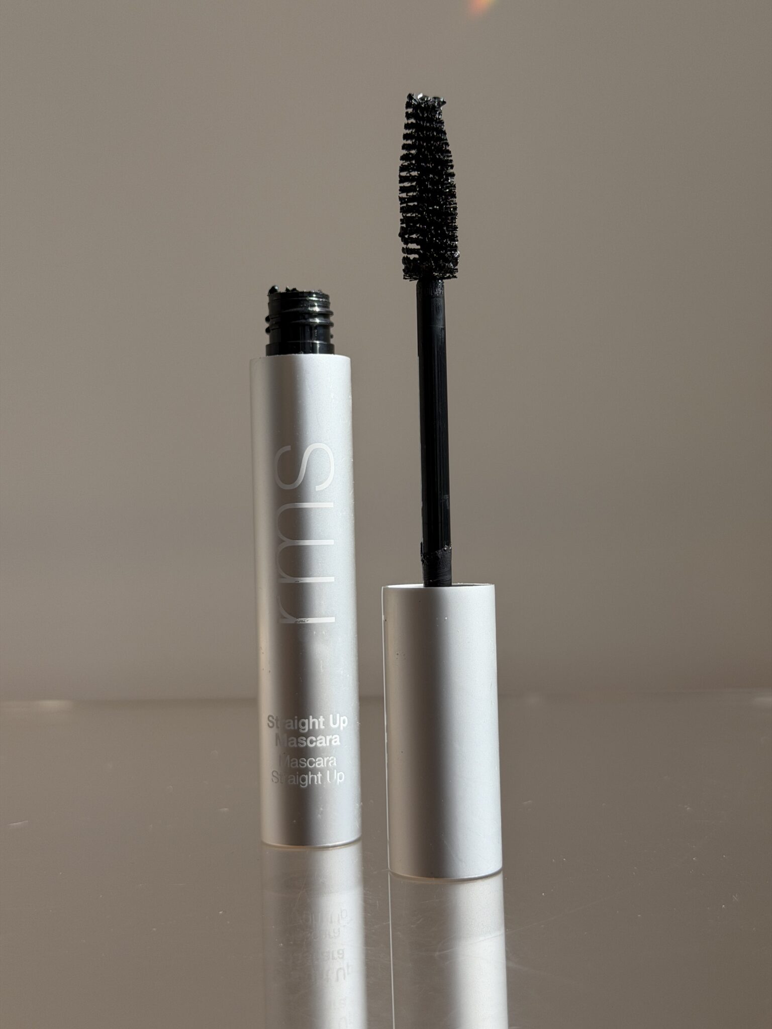 An open tube of RMS mascara with the wand standing upright next to the silver container, photographed against a plain background.