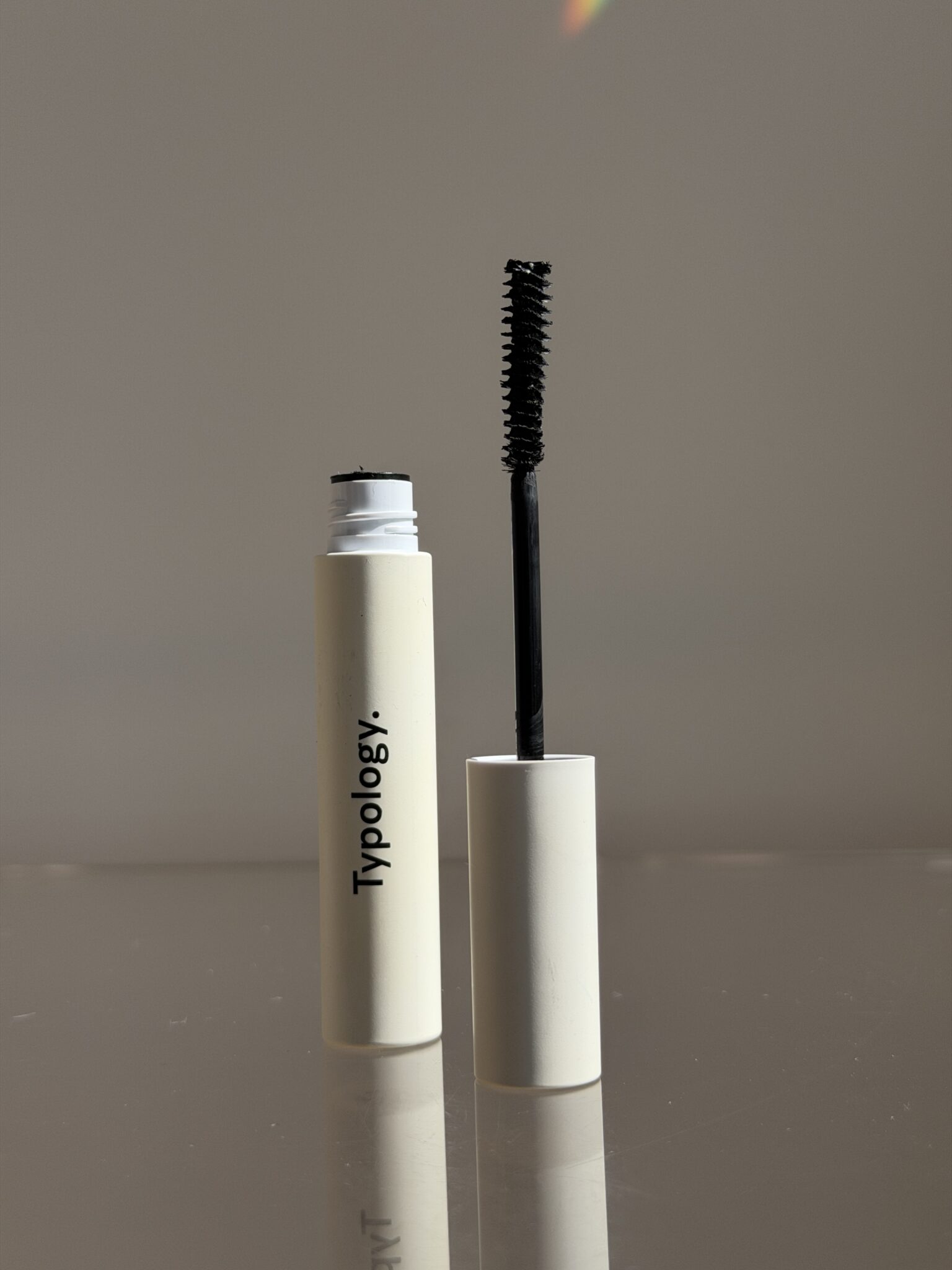 A tube of mascara with the wand removed and standing upright beside it, labeled "Typology," set against a plain background.