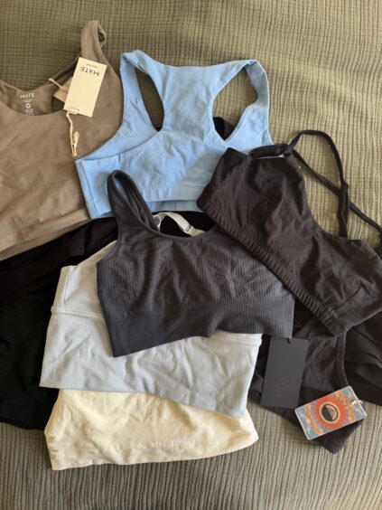 Several sports bras and bralettes in various colors, including blue, black, brown, and beige, are laid out on a textured fabric surface, some with tags attached.