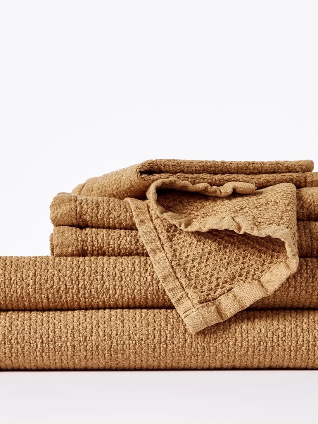 A neatly folded stack of tan-colored organic towels with a textured finish is arranged against a plain white background.