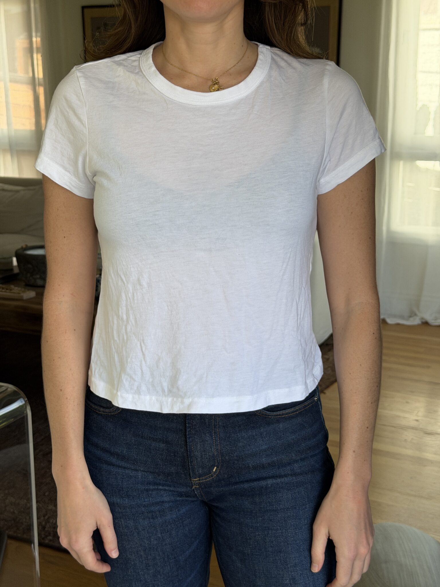 A person standing indoors wearing a plain white short-sleeve t-shirt and dark blue jeans.