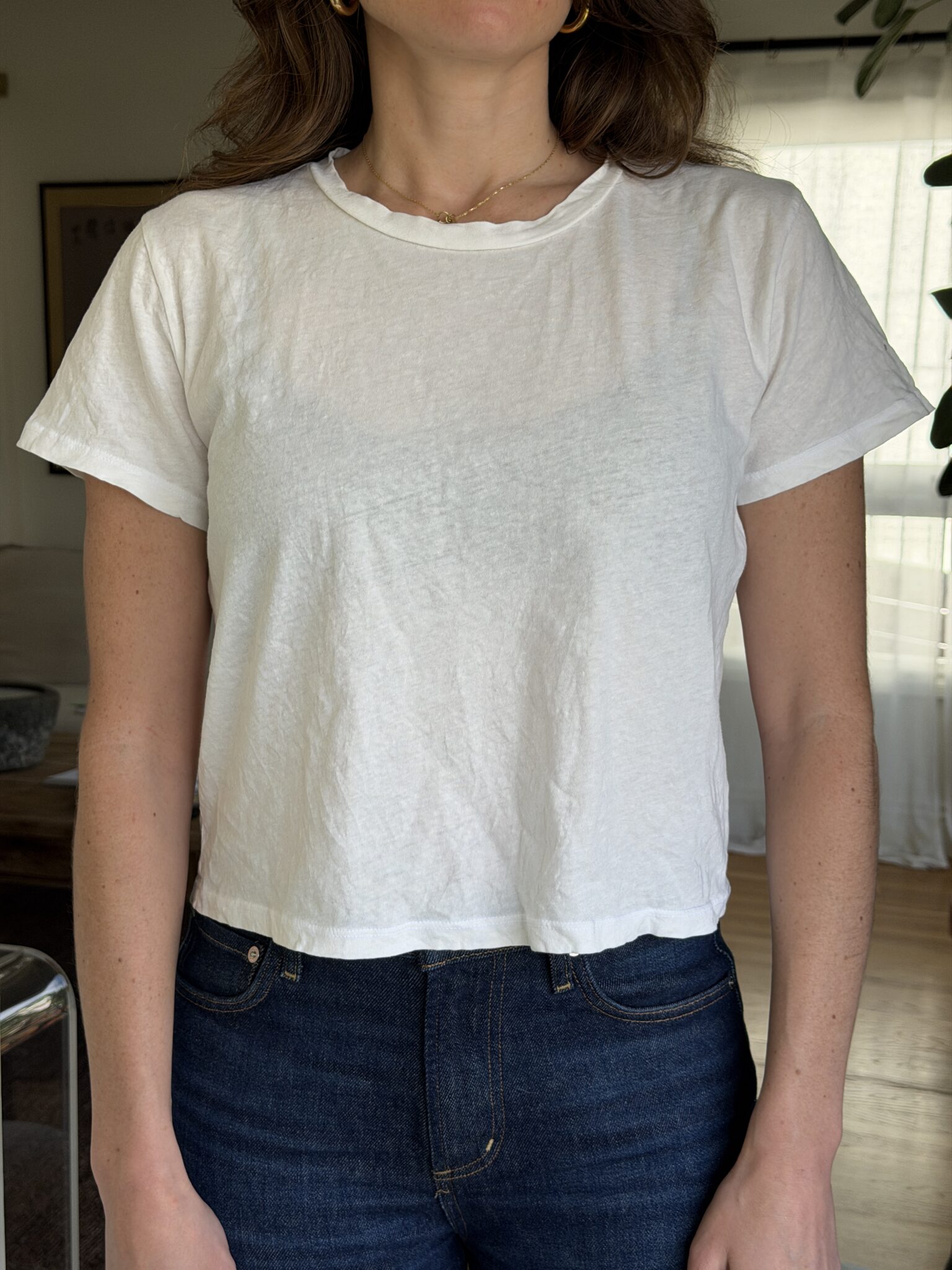 A person wearing a plain white short-sleeve t-shirt and dark blue jeans stands indoors in a well-lit room.