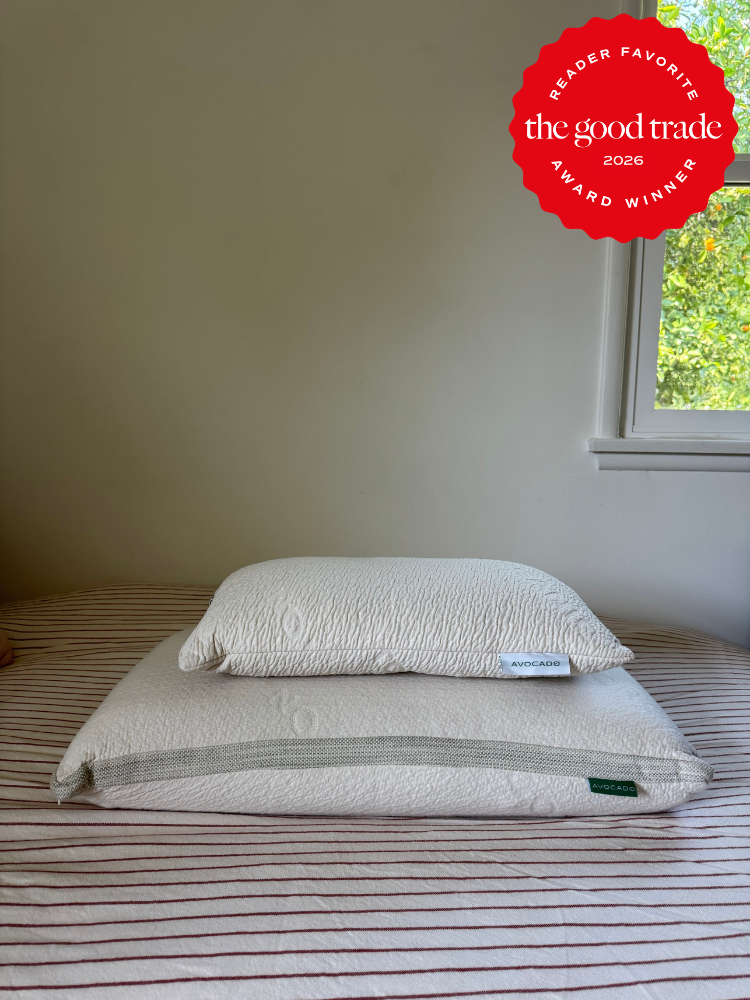 Two stacked white pillows on a striped bedspread near a window, with a "The Good Trade Award Winner 2026 Reader Favorite" badge in the upper right corner.