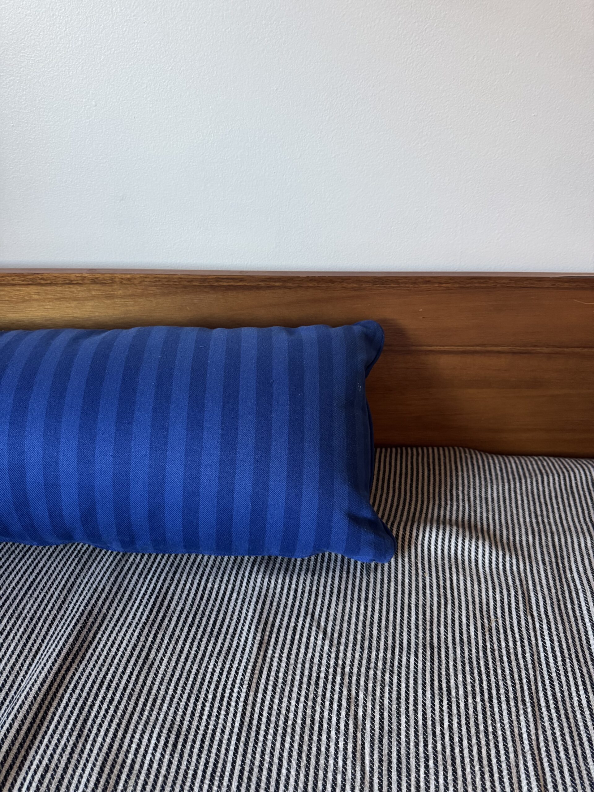A blue striped pillow rests against a wooden headboard on a bed with a black-and-white striped blanket.