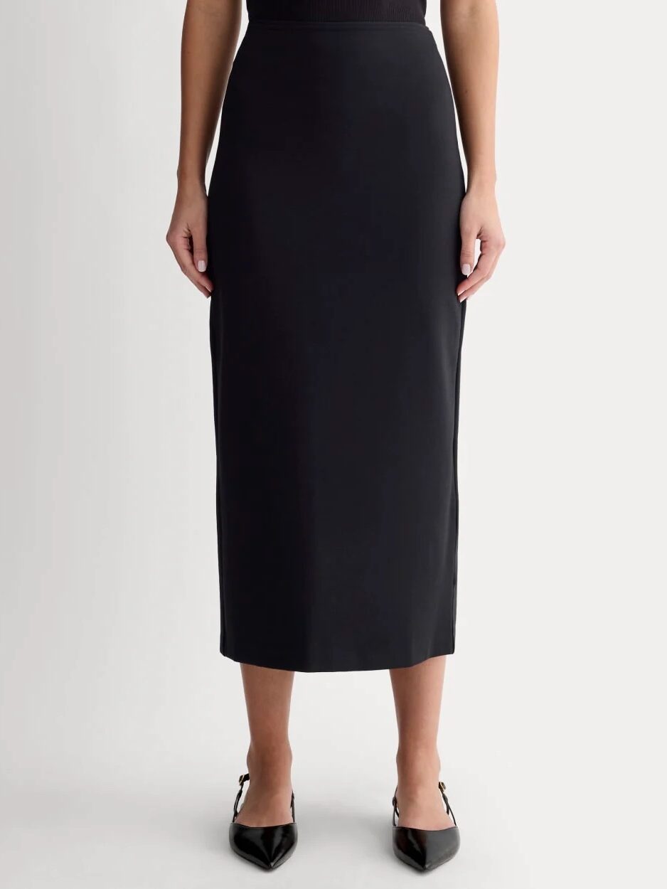 A person wearing a black, high-waisted, ankle-length skirt and black pointed-toe shoes, standing against a plain white background.