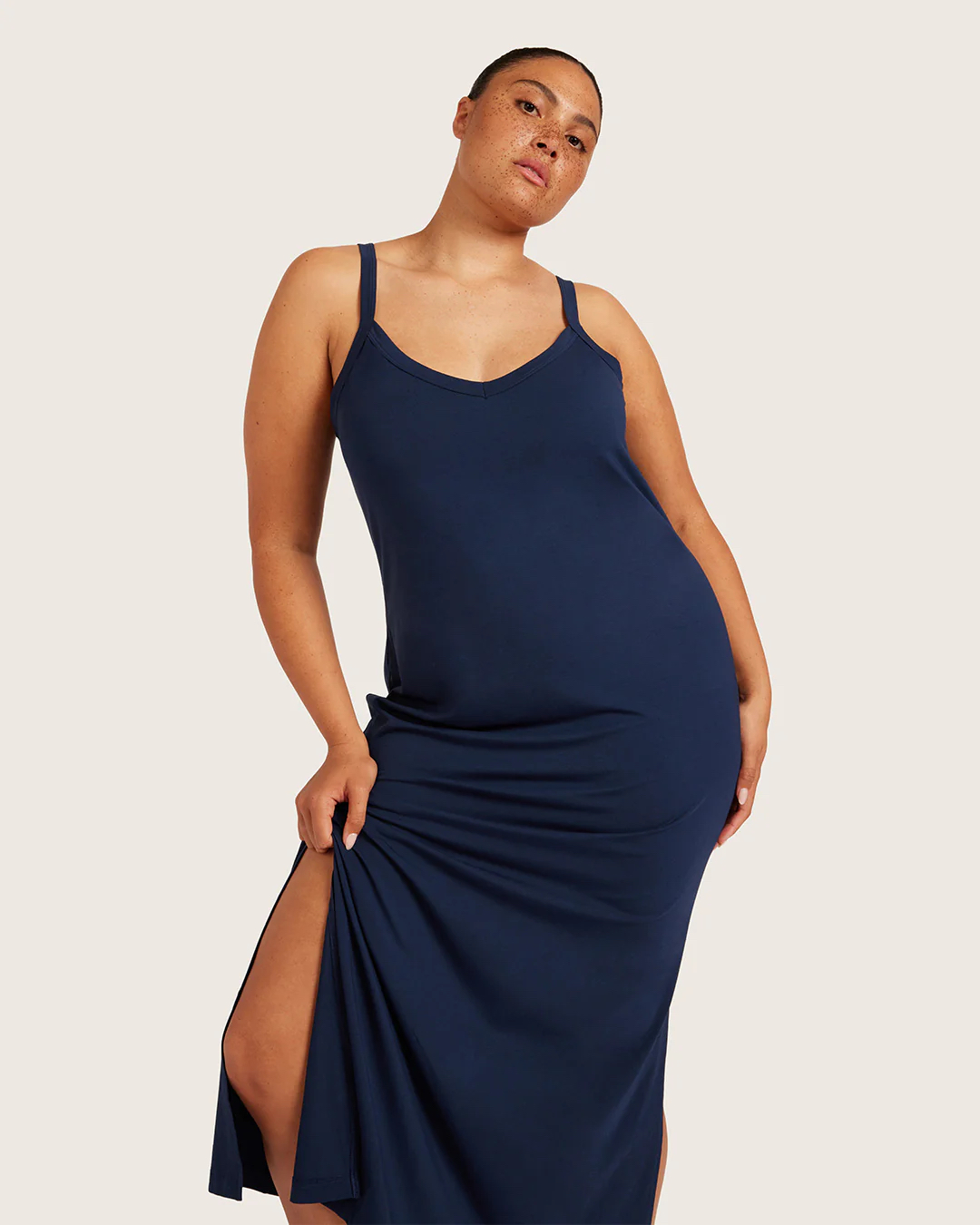 Person in a navy blue sleeveless maxi dress with a side slit poses against a plain light background.