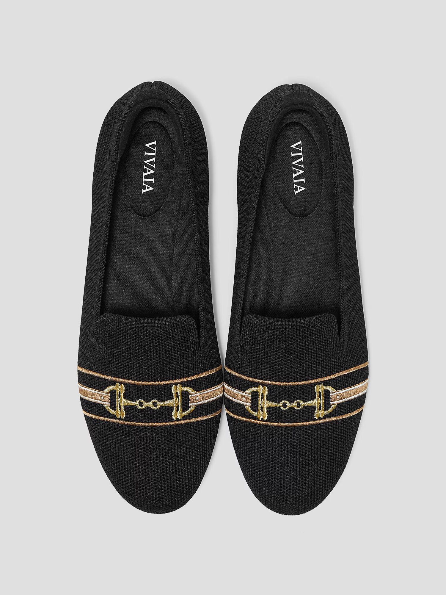 A pair of black VIVAIA slip-on shoes with gold embroidered horsebit detailing on the front, shown from above against a light gray background.