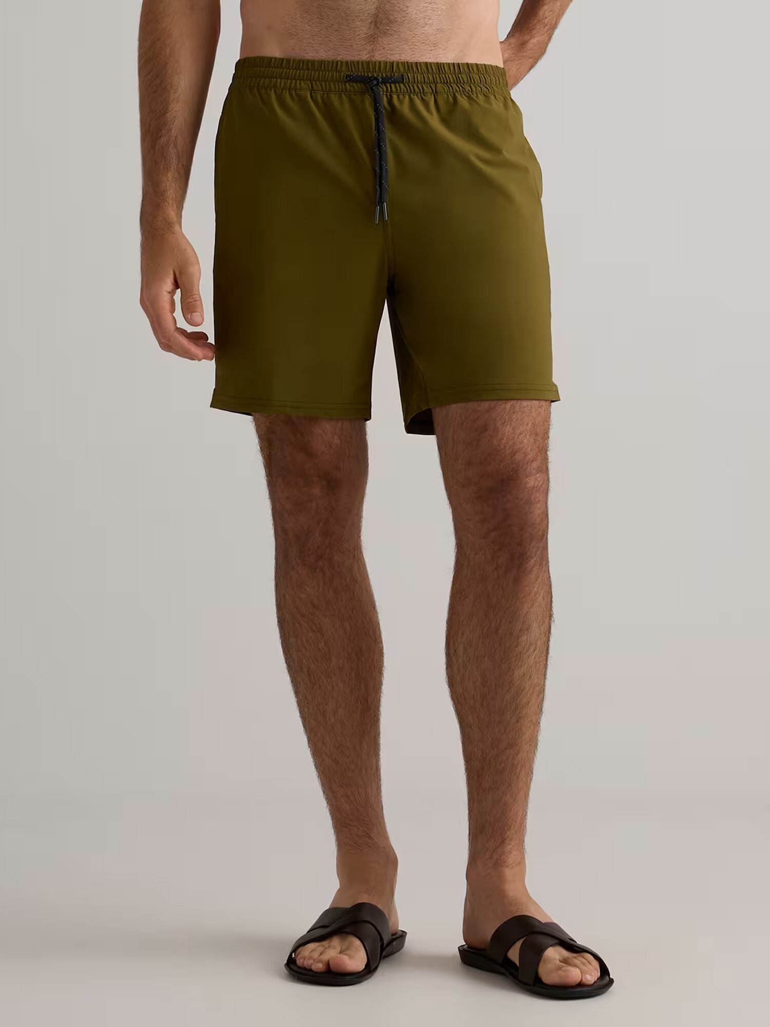 A person wearing olive green shorts with a black drawstring and brown sandals, standing against a plain background.