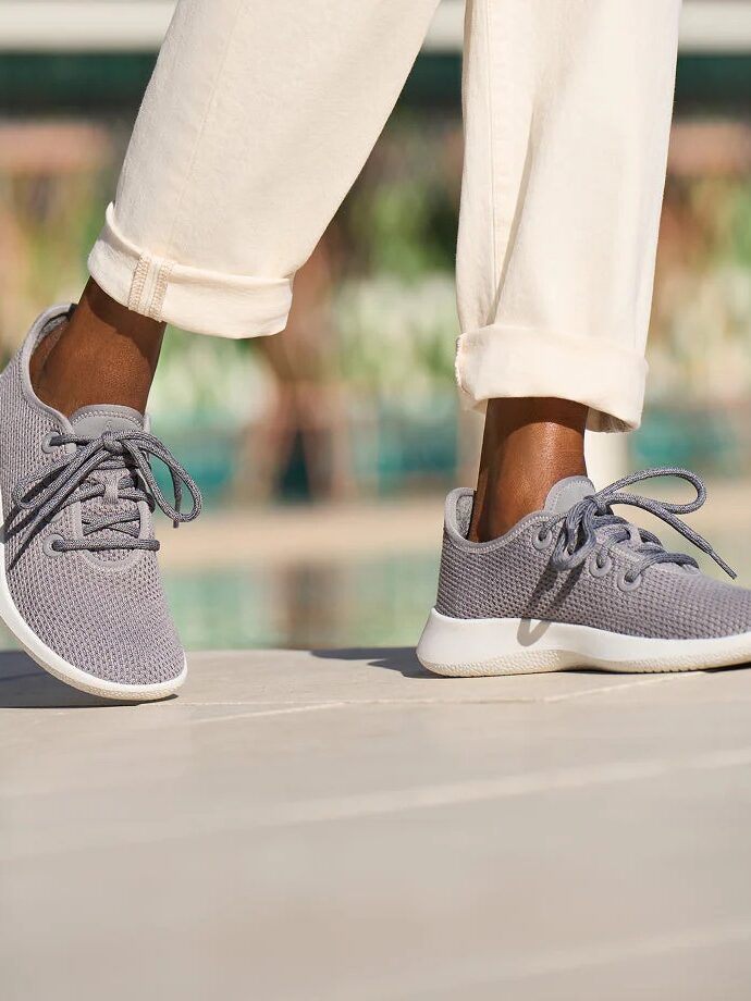 A person wearing light gray sustainable sneakers and cream-colored pants stands on an outdoor surface.