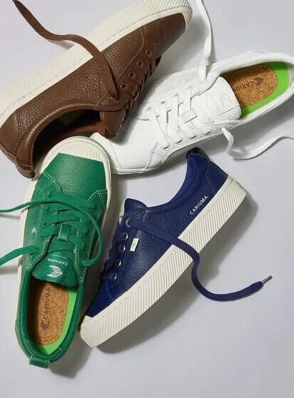 Four pairs of sustainable sneakers in brown, green, navy, and white on the left; a person wearing white sneakers and blue socks stands on a stone block on the right.