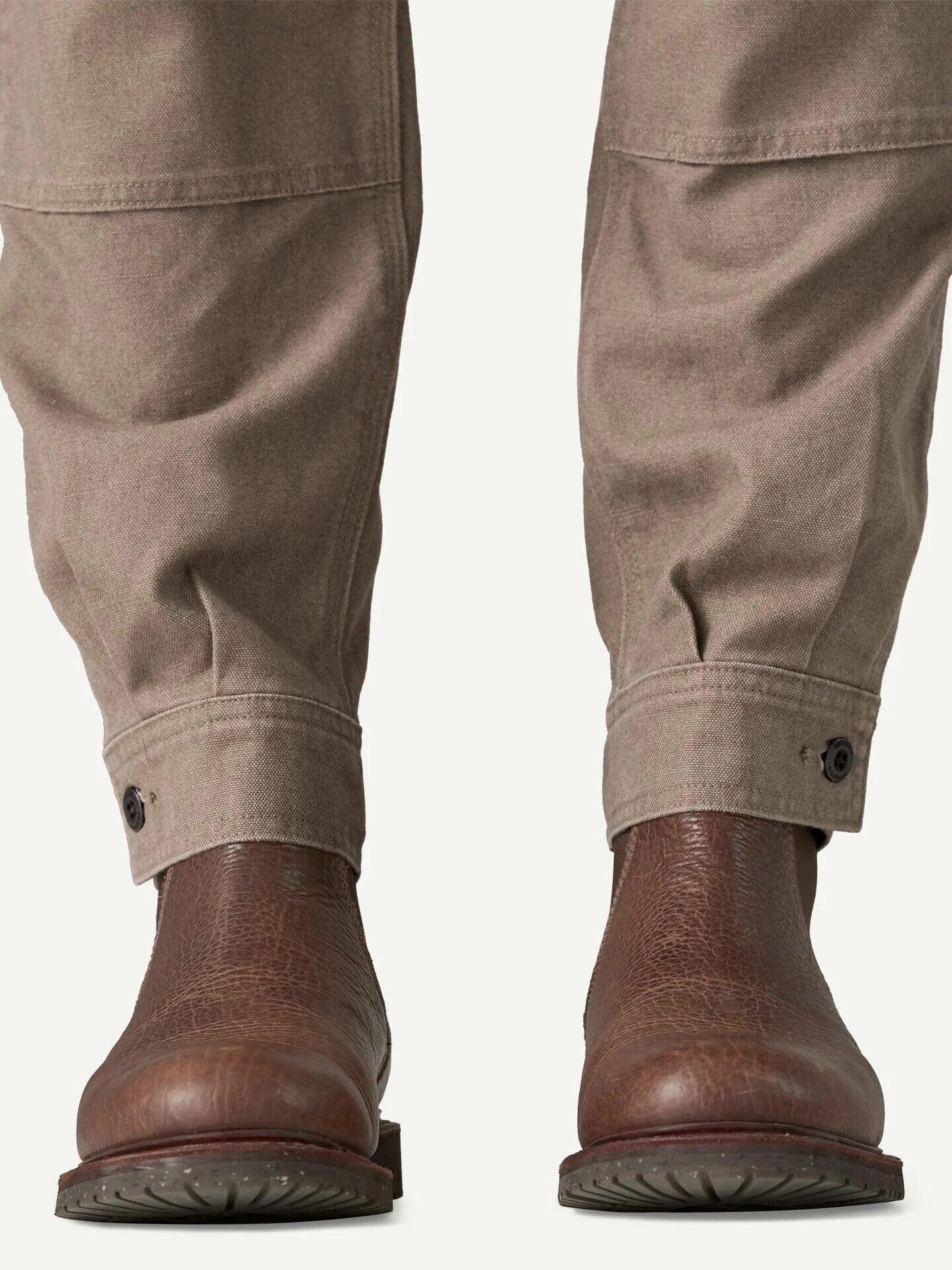 A person wearing light brown pants with buttoned cuffs and brown leather boots, shown from the knees down against a plain background.