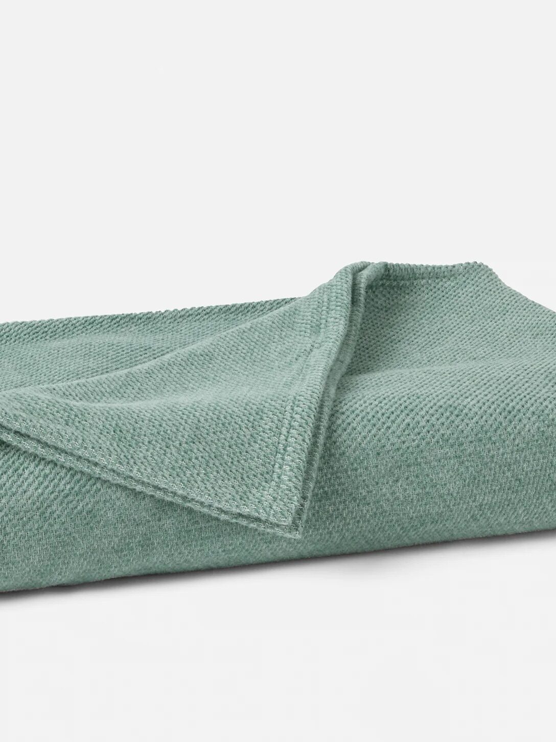 A neatly folded, textured light green blanket is placed on a plain white background.