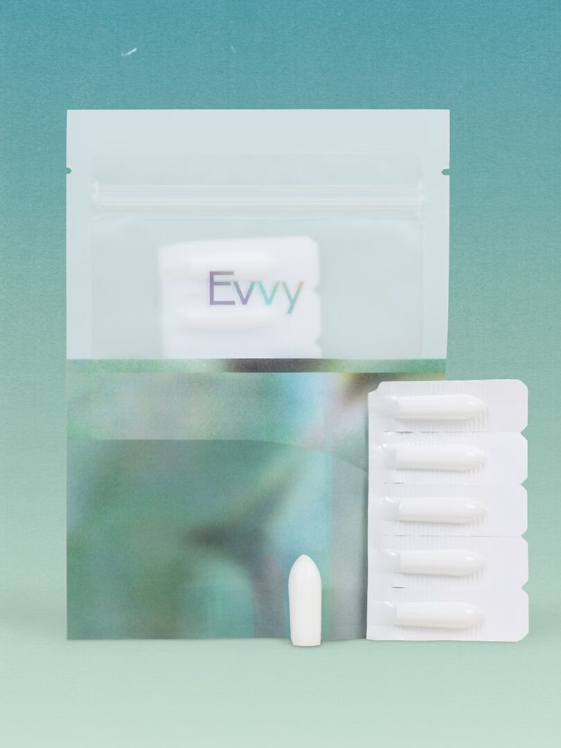 A white suppository and a blister pack of suppositories are displayed in front of a ziplock pouch labeled "Evvy" against a gradient blue-green background.