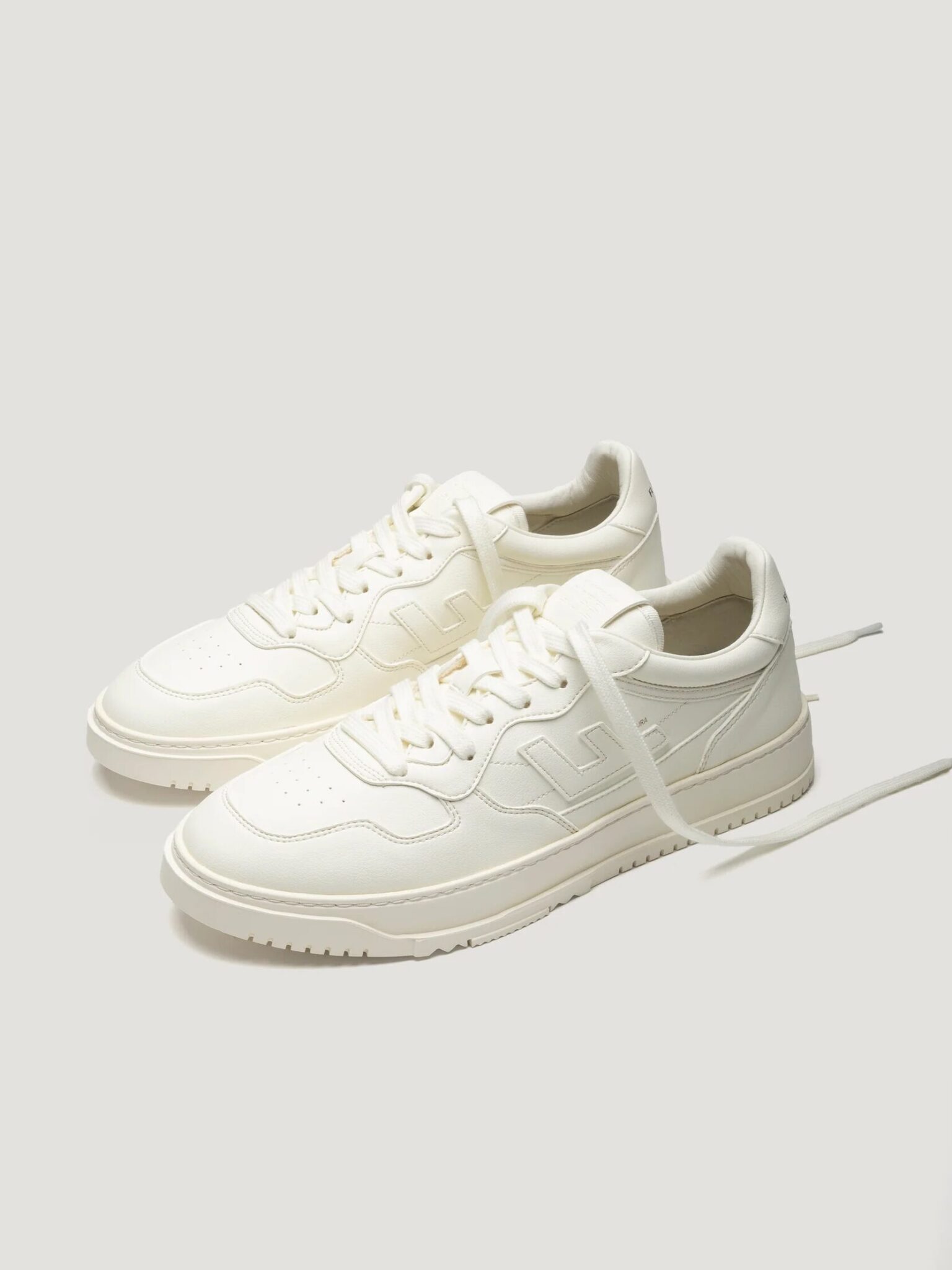A pair of off-white low-top sneakers with laces, side stitching details, and textured rubber soles, shown on a plain light background.