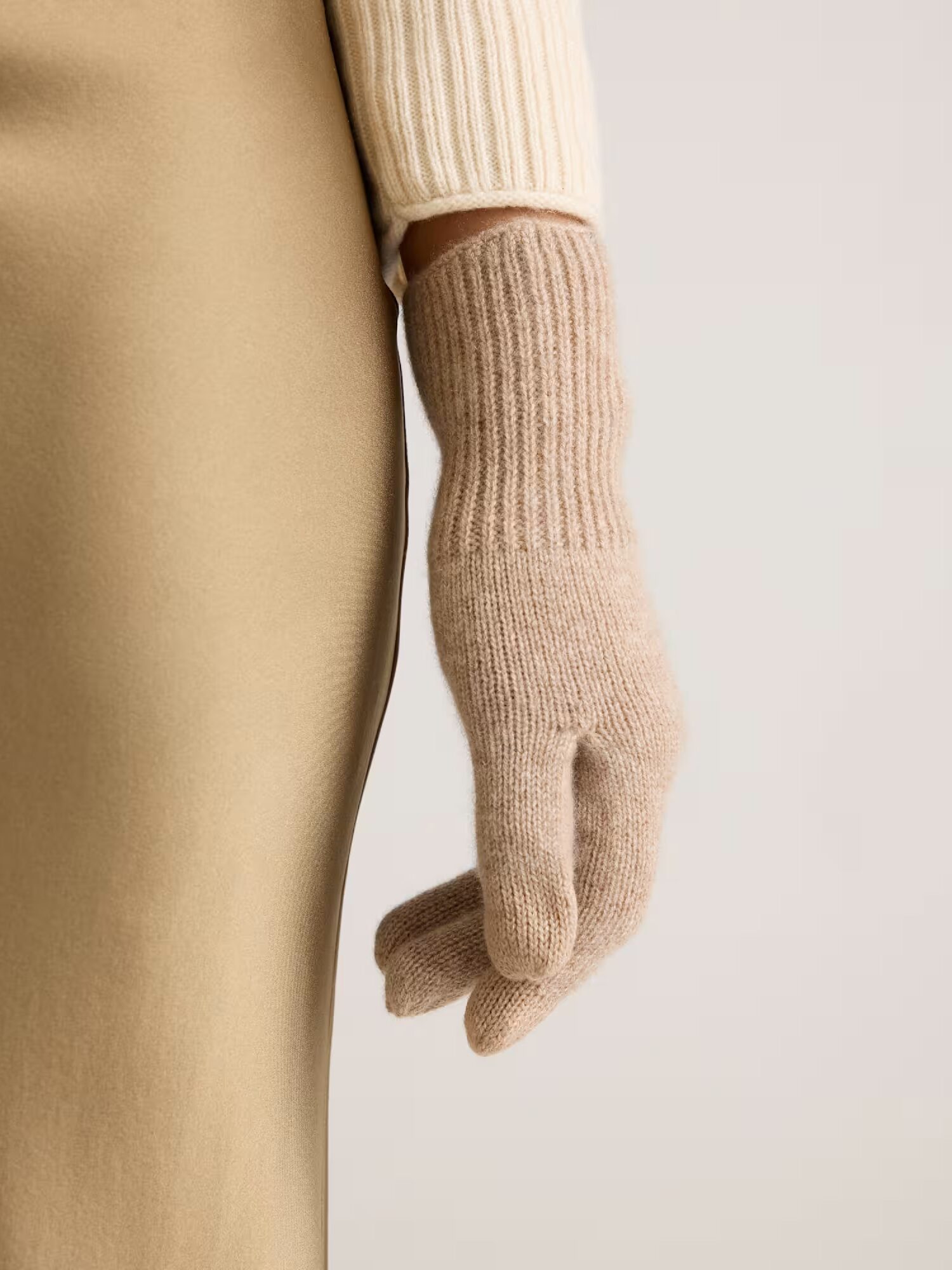 A person wearing a beige knit glove, a cream ribbed sweater, and a gold satin skirt, shown from the waist down against a plain background.