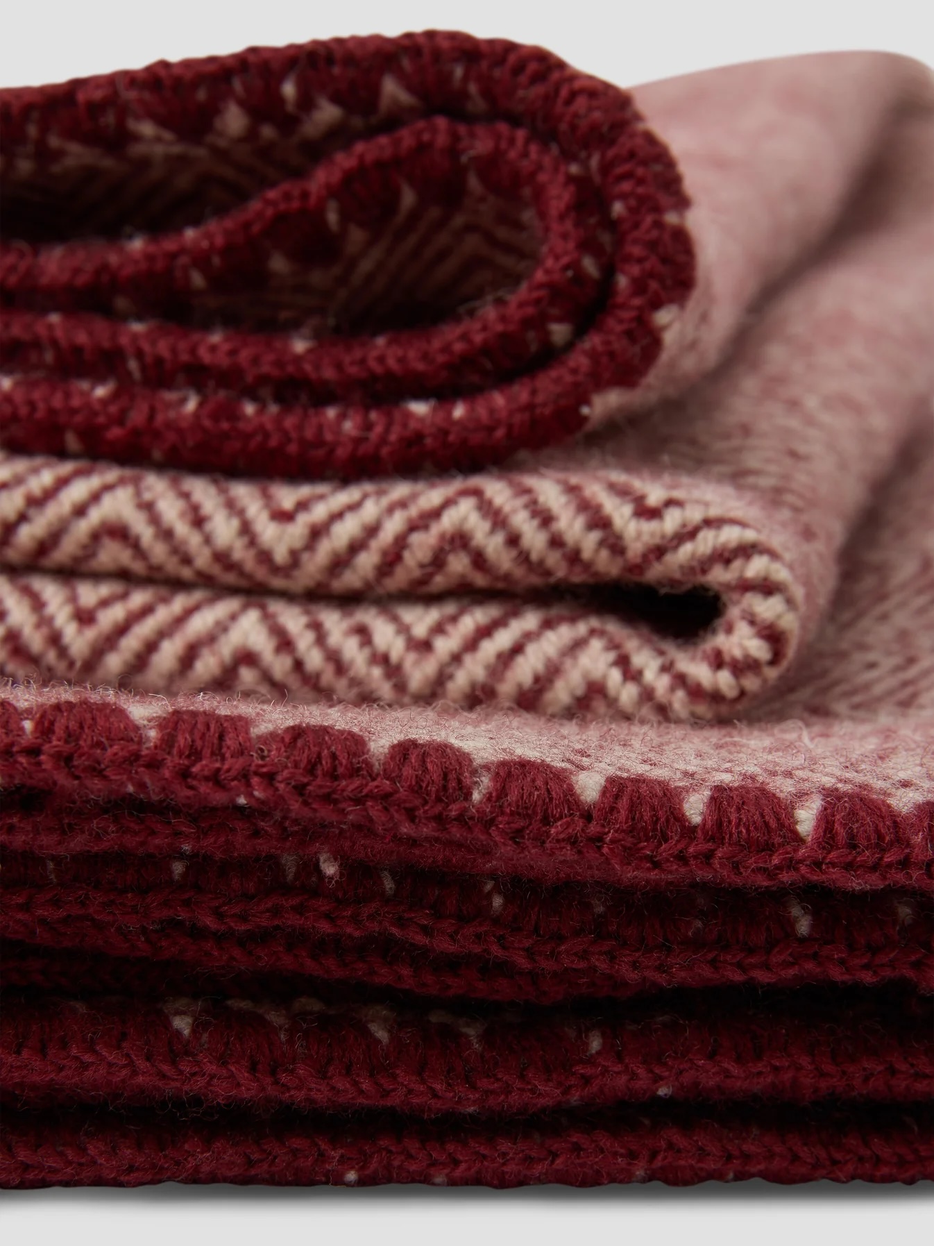 A close-up of folded maroon and beige wool blankets with a chevron pattern and crocheted trim.