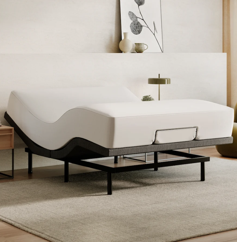 A modern adjustable bed with a white mattress is elevated at the head and foot, positioned in a minimalist bedroom with neutral decor and a beige rug.