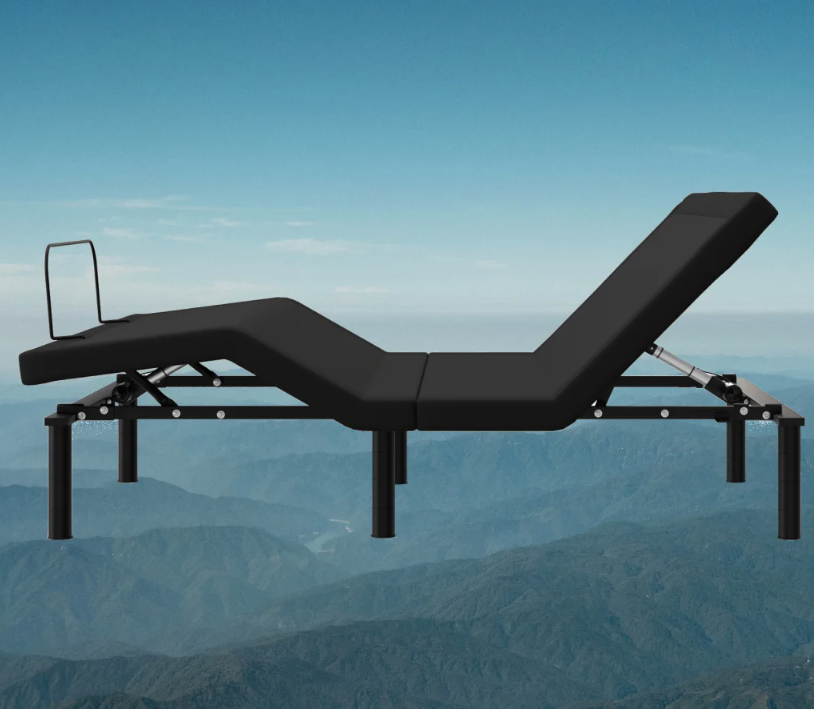 A black adjustable bed frame with elevated head and foot sections, set against a backdrop of mountains and a clear blue sky.