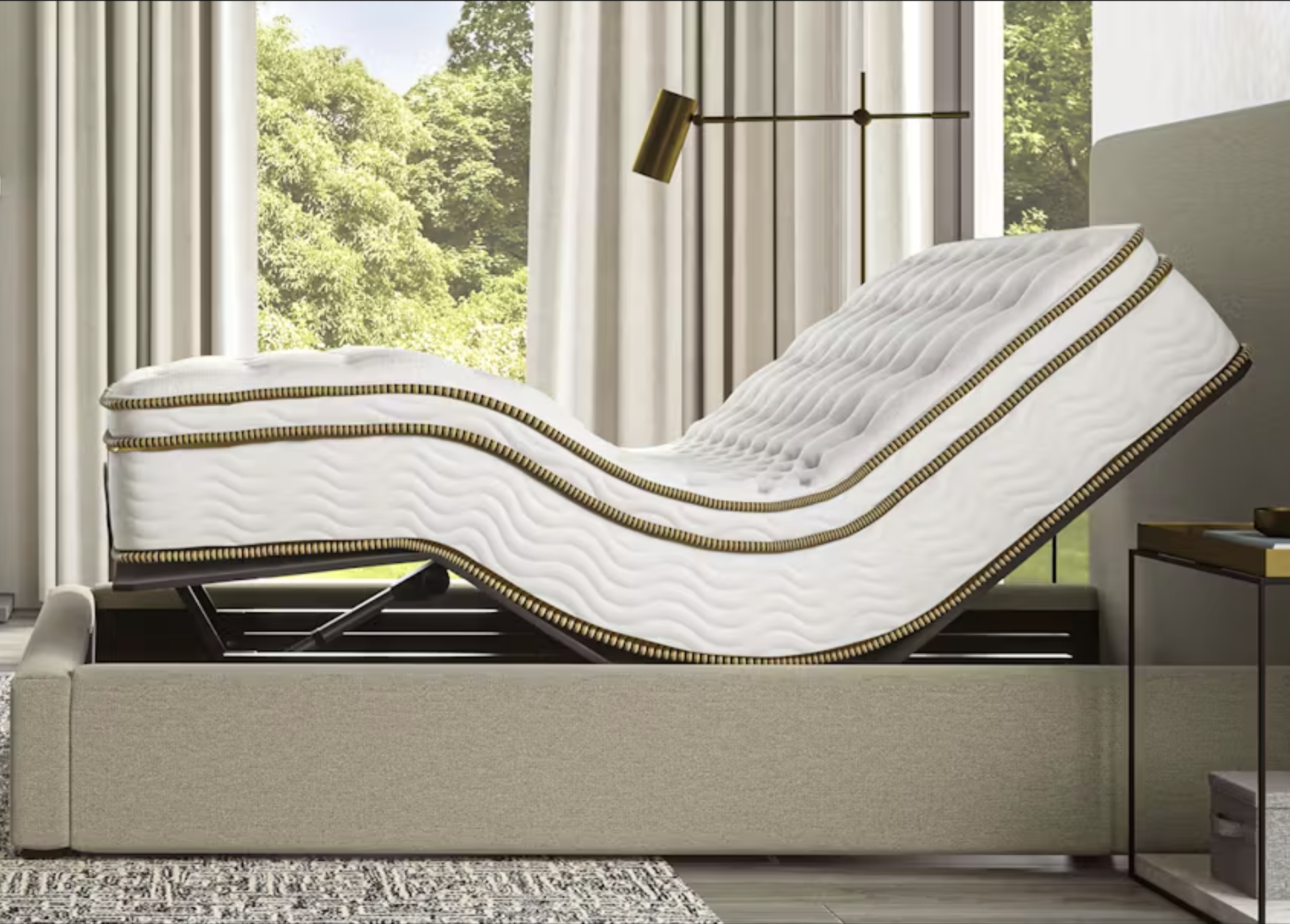 An adjustable bed with a white and gold mattress is shown in a partially elevated position in a modern bedroom with large windows and neutral decor.