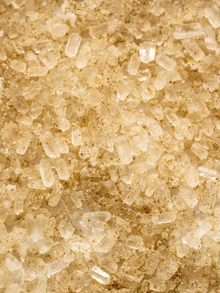 Close-up of uncooked white rice grains mixed with brown specks, possibly seasoning or spices, spread out in an even layer.