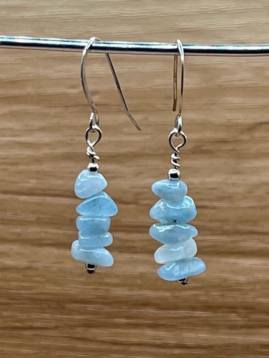 A pair of dangle earrings with light blue irregular stone beads stacked vertically on metal hooks, displayed against a wooden background.