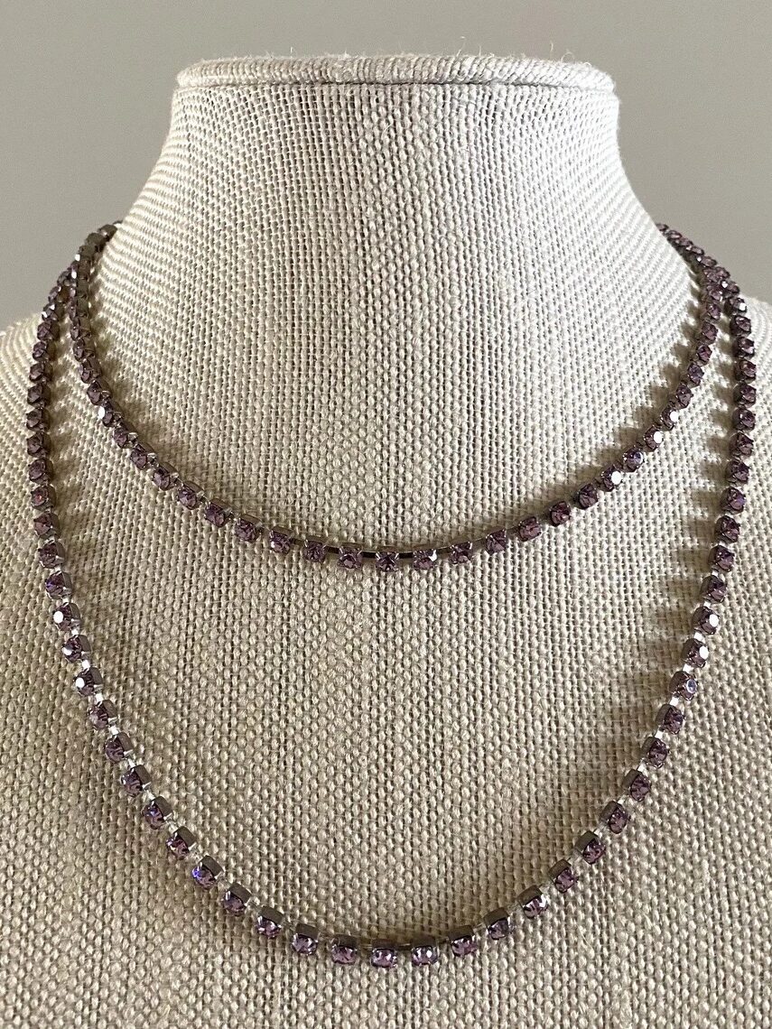 A double-layered necklace with small, round purple gemstones displayed on a beige fabric bust against a plain background.