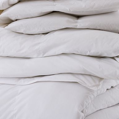 A stack of white comforters or duvets folded neatly on top of each other.