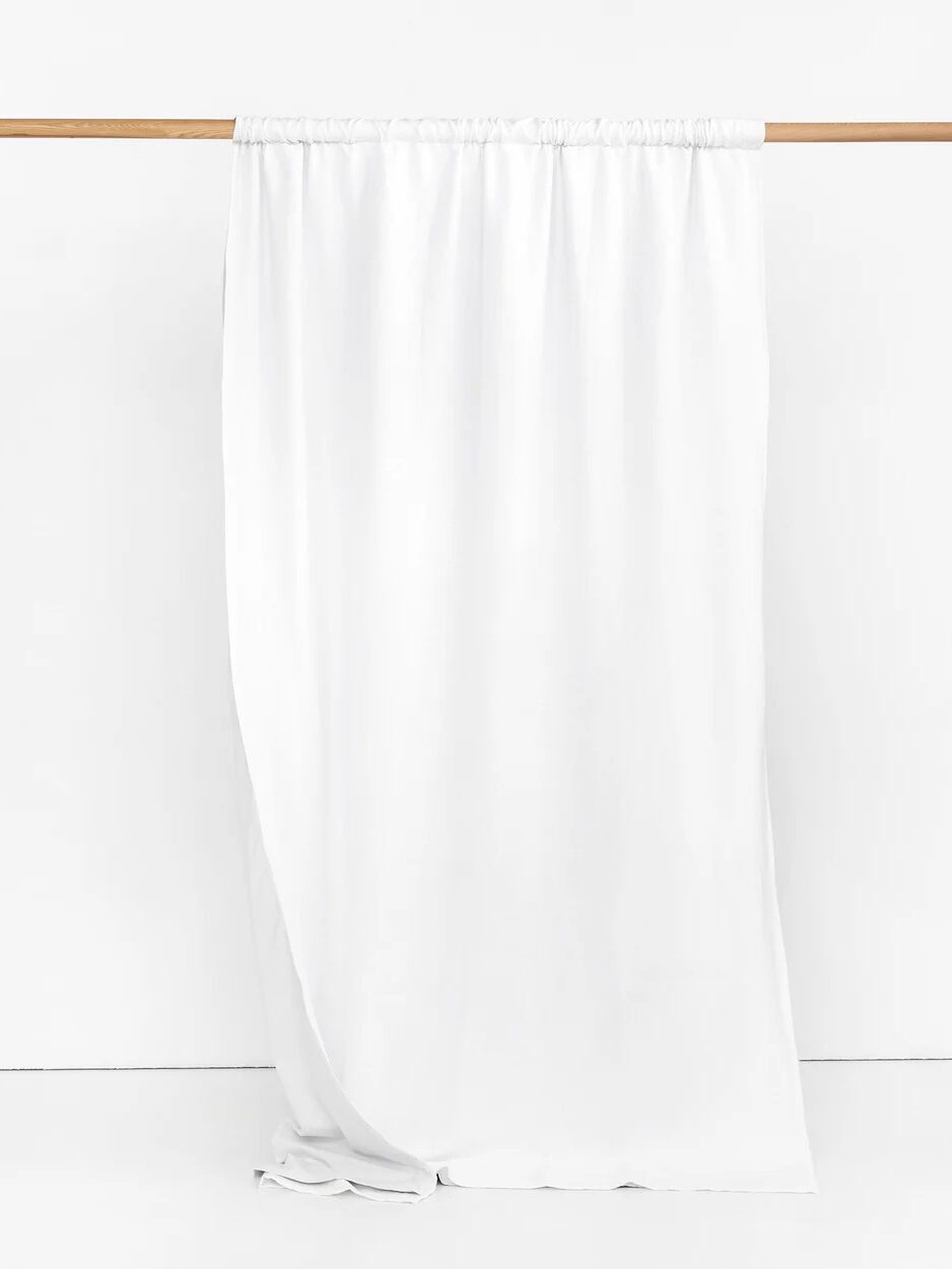 A long, plain white curtain hangs from a wooden rod against a white background.