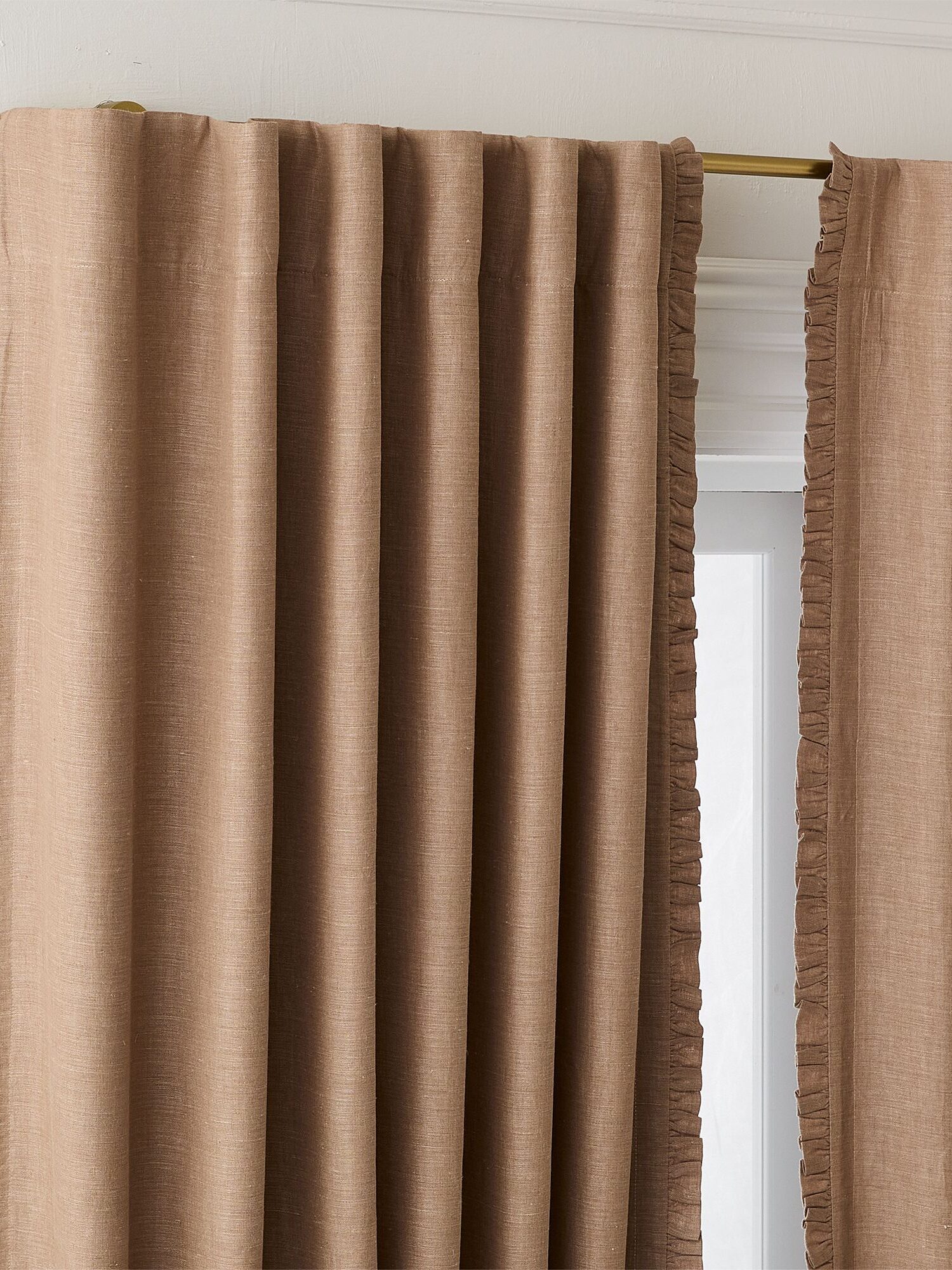 Brown curtains with ruffled edges hang on a brass curtain rod, partially covering a white window frame.