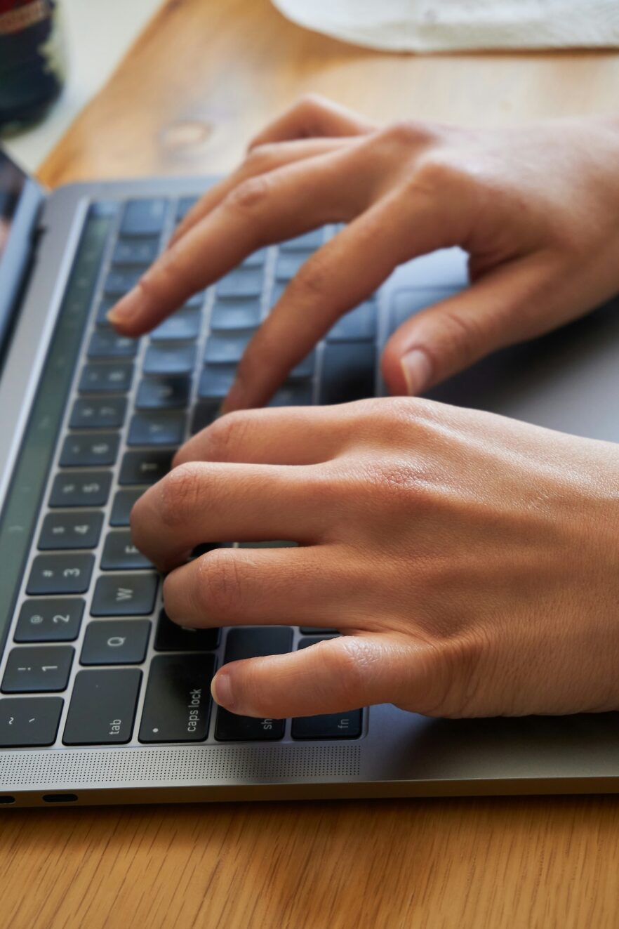 Close-up of two hands typing on a laptop keyboard on a wooden surface.