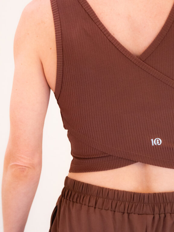 Close-up of a person's back wearing a ribbed, sleeveless brown crop top with a wrap design and brown elastic waistband pants.