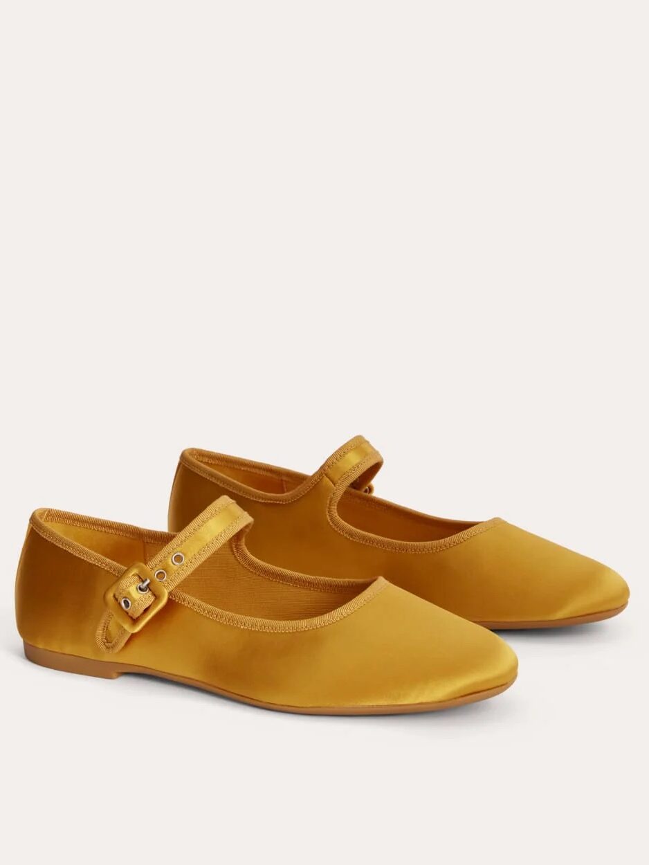A pair of mustard yellow satin Mary Jane flats with a buckle strap, displayed on a light background.