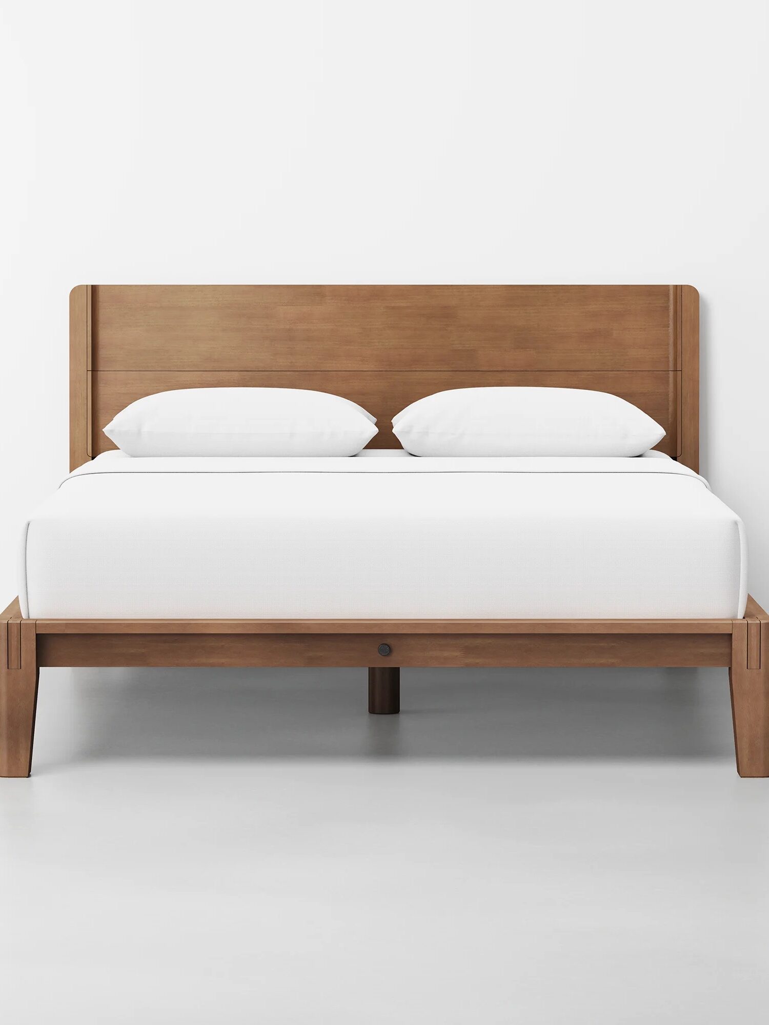 A wooden bed frame with a headboard, neatly made with white bedding and two white pillows, placed in a minimalistic room with a white wall and floor.