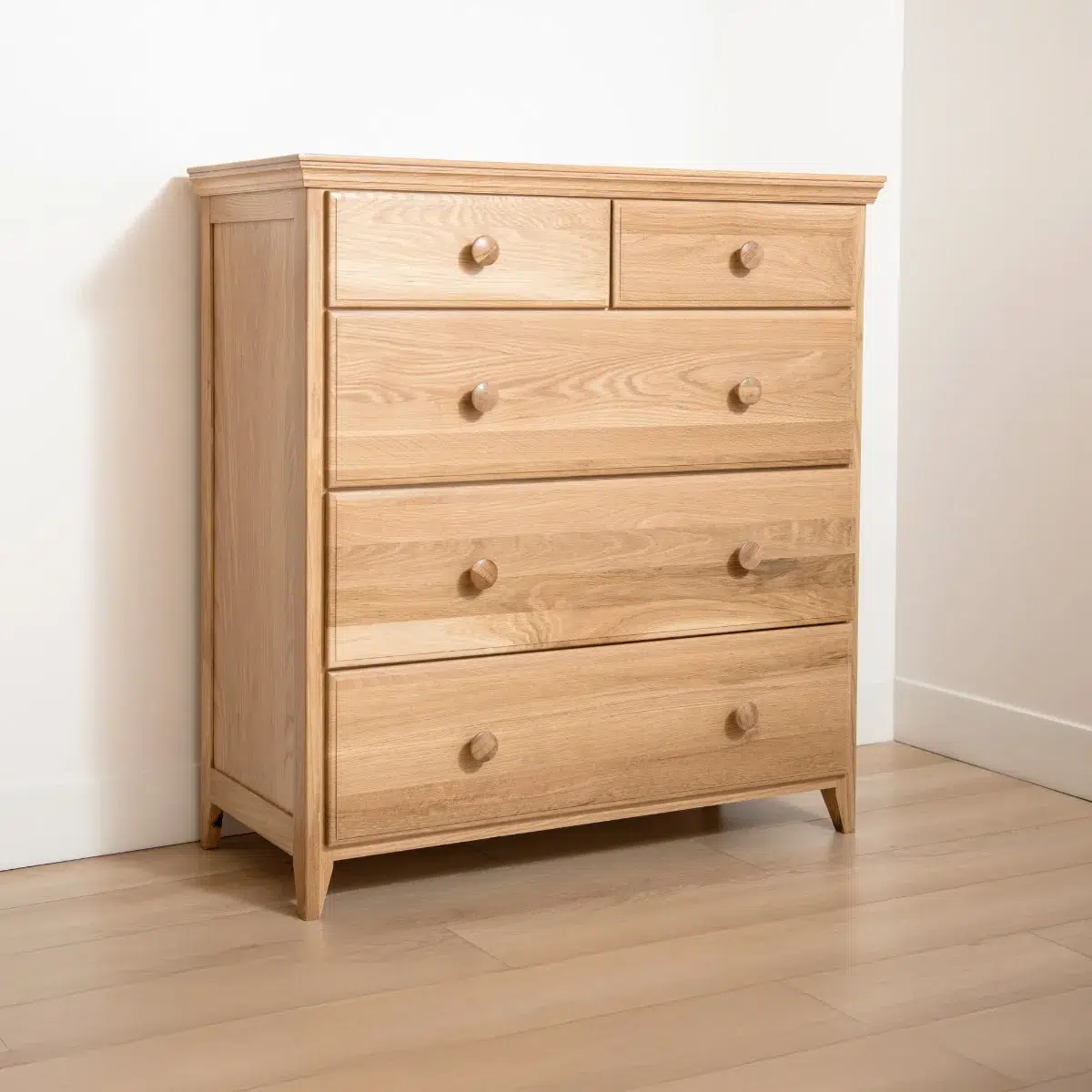 A light wood dresser with five drawers, two smaller on top and three larger below, standing on a hardwood floor against a white wall in a corner.
