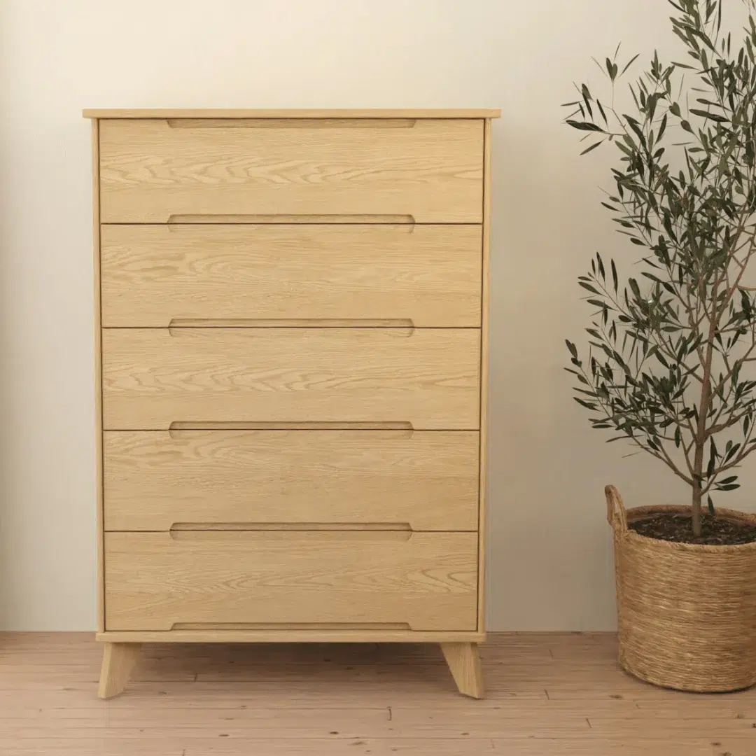 A light wood dresser with six drawers stands next to a potted plant in a woven basket on a wooden floor against a plain light-colored wall.