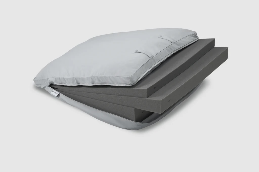 A gray pillow with its cover partially unzipped, revealing three stacked layers of black foam inside.