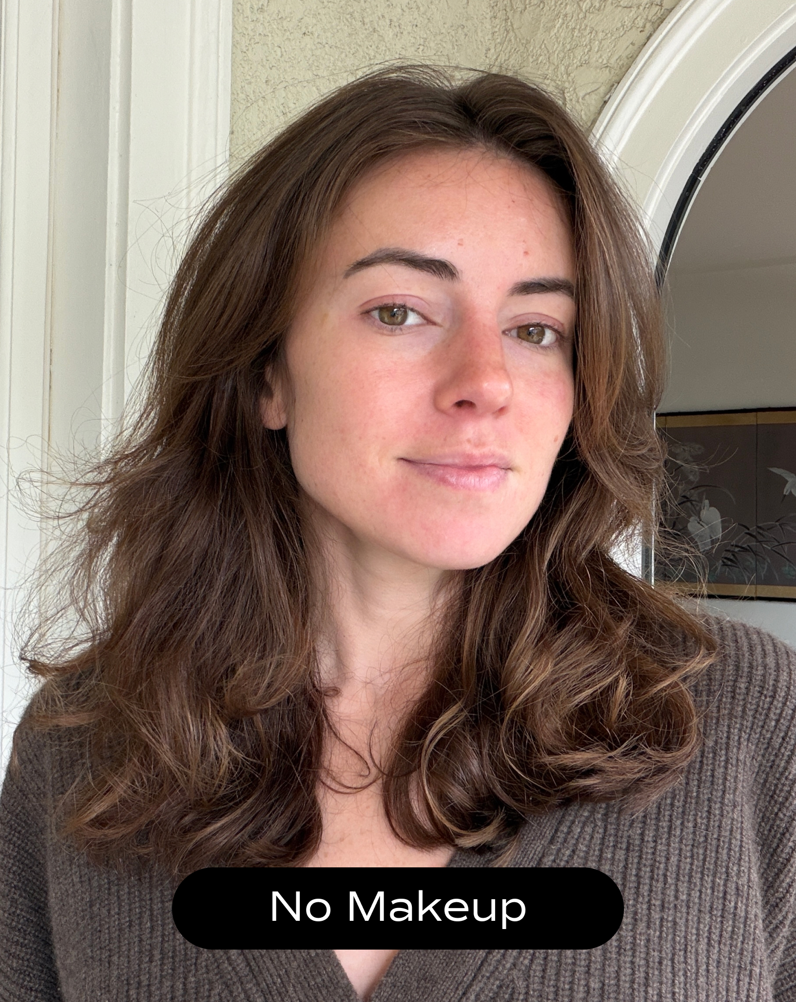 A woman with medium-length brown hair and clear skin looks at the camera, wearing a brown sweater. The caption reads "No Makeup.