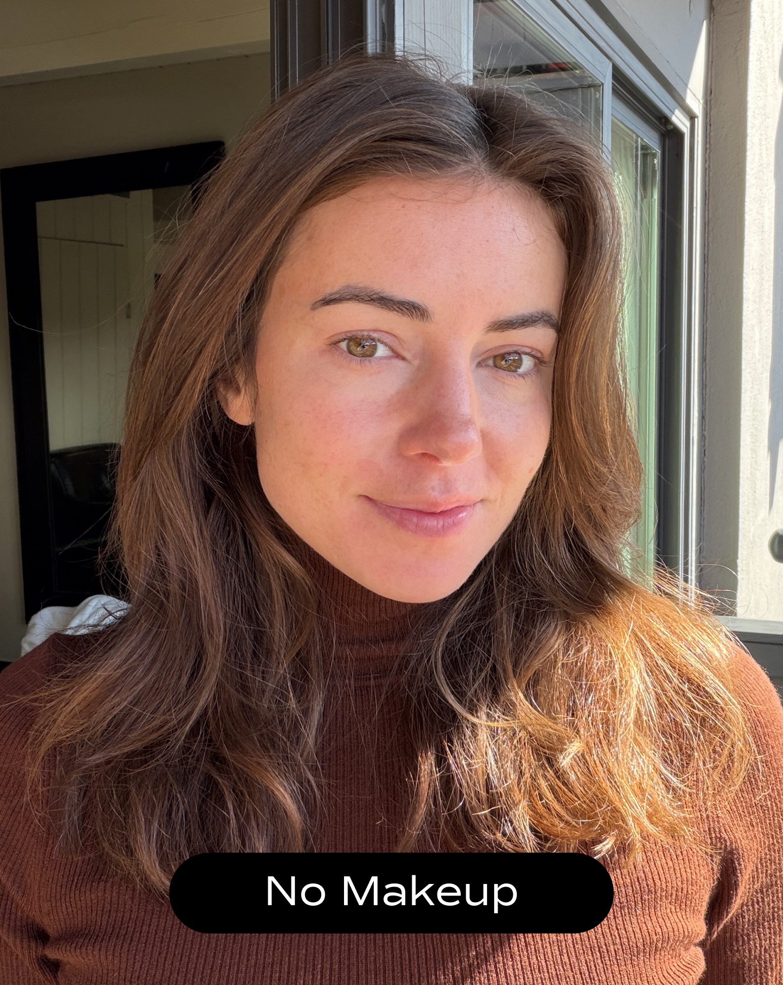 A woman with long brown hair wearing a brown turtleneck stands by a window in natural light. The text on the image reads "No Makeup.